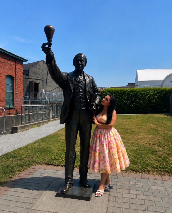 Nabiha Yousuf beside a bronze statue of Thomas Edison holding a lightbulb